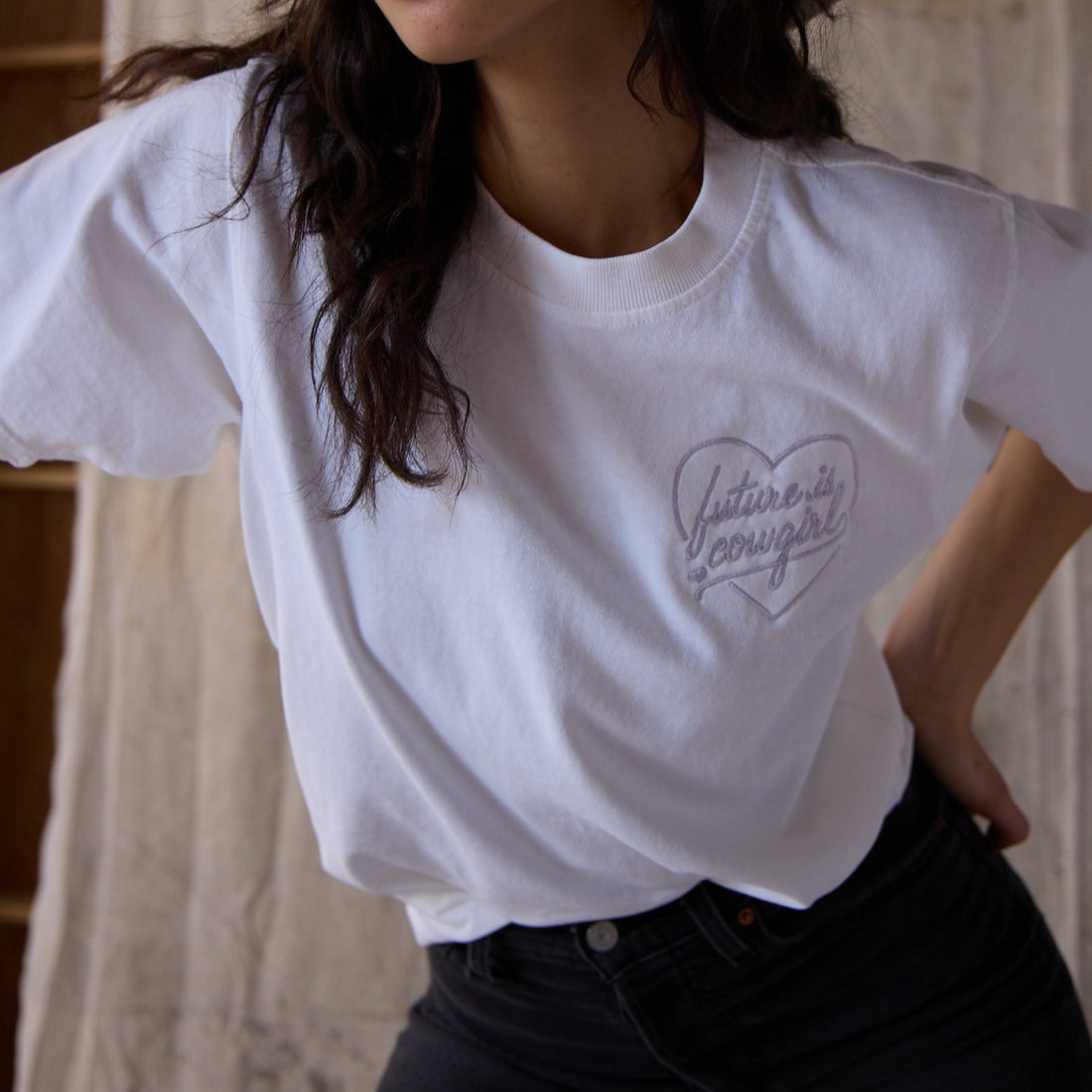 A woman wearing a white t shirt with an embroidered heart future is cowgirl logo