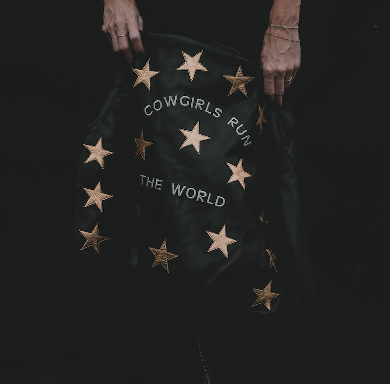 A black bomber jacket with metallic gold stars and text 'Cowgirls Run the World' on the back.