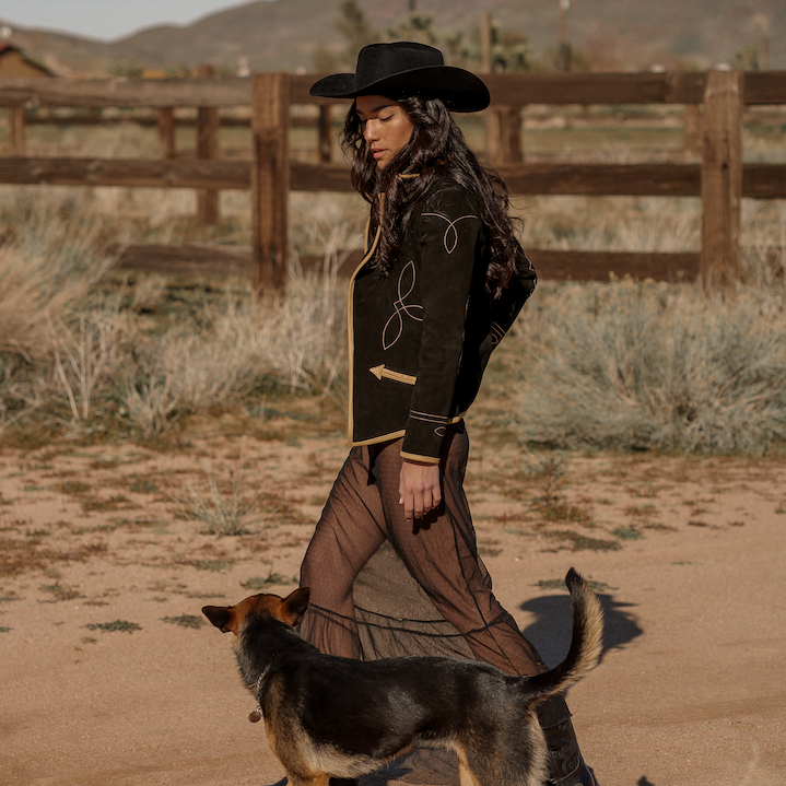 A woman wearing a black suede blazer with tan leather details paired with a black hat