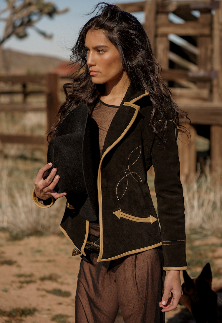 A woman wearing a black suede blazer with tan leather details paired with a black hat