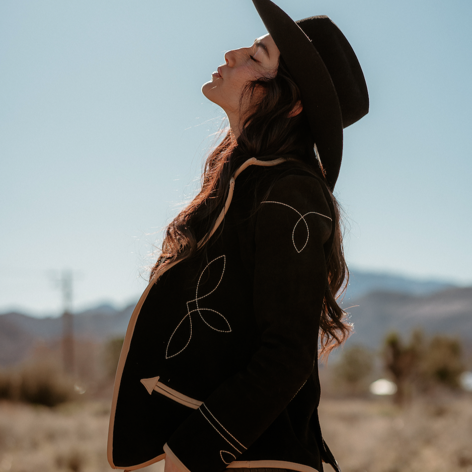 A woman wearing a black suede blazer with tan leather details paired with a black hat
