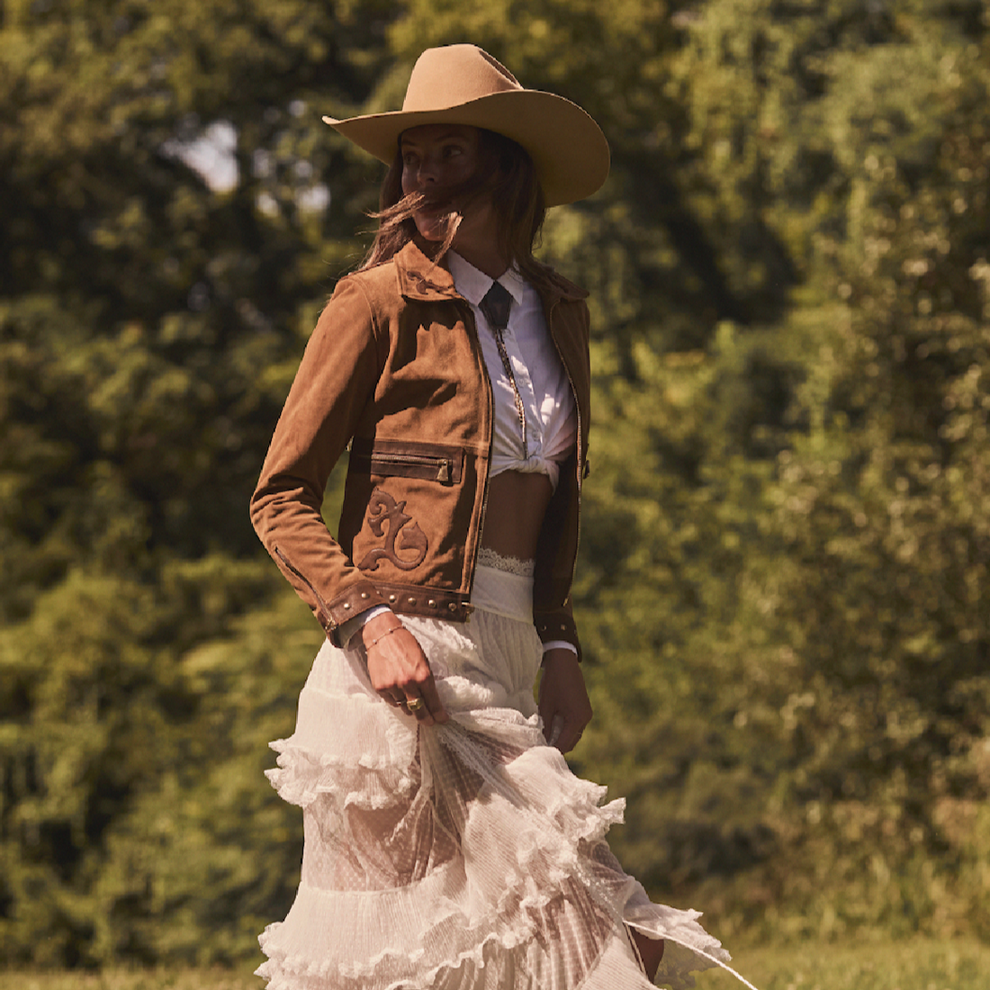 Woman wearing a cowboy hat and brown embroidered jacket by Western & Co in a natural outdoor setting