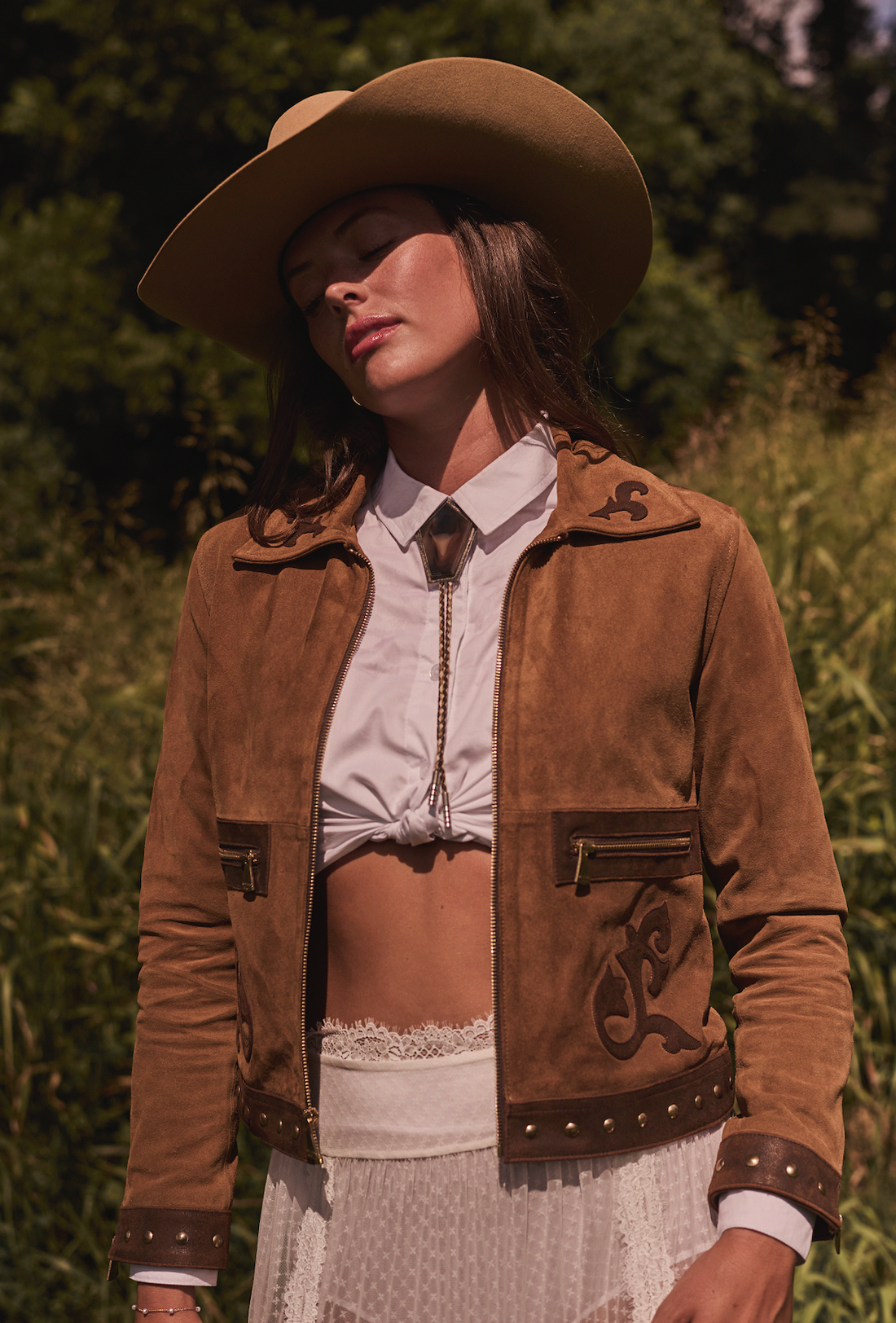 Woman wearing a cowboy hat and brown embroidered jacket by Western & Co in a grassy field