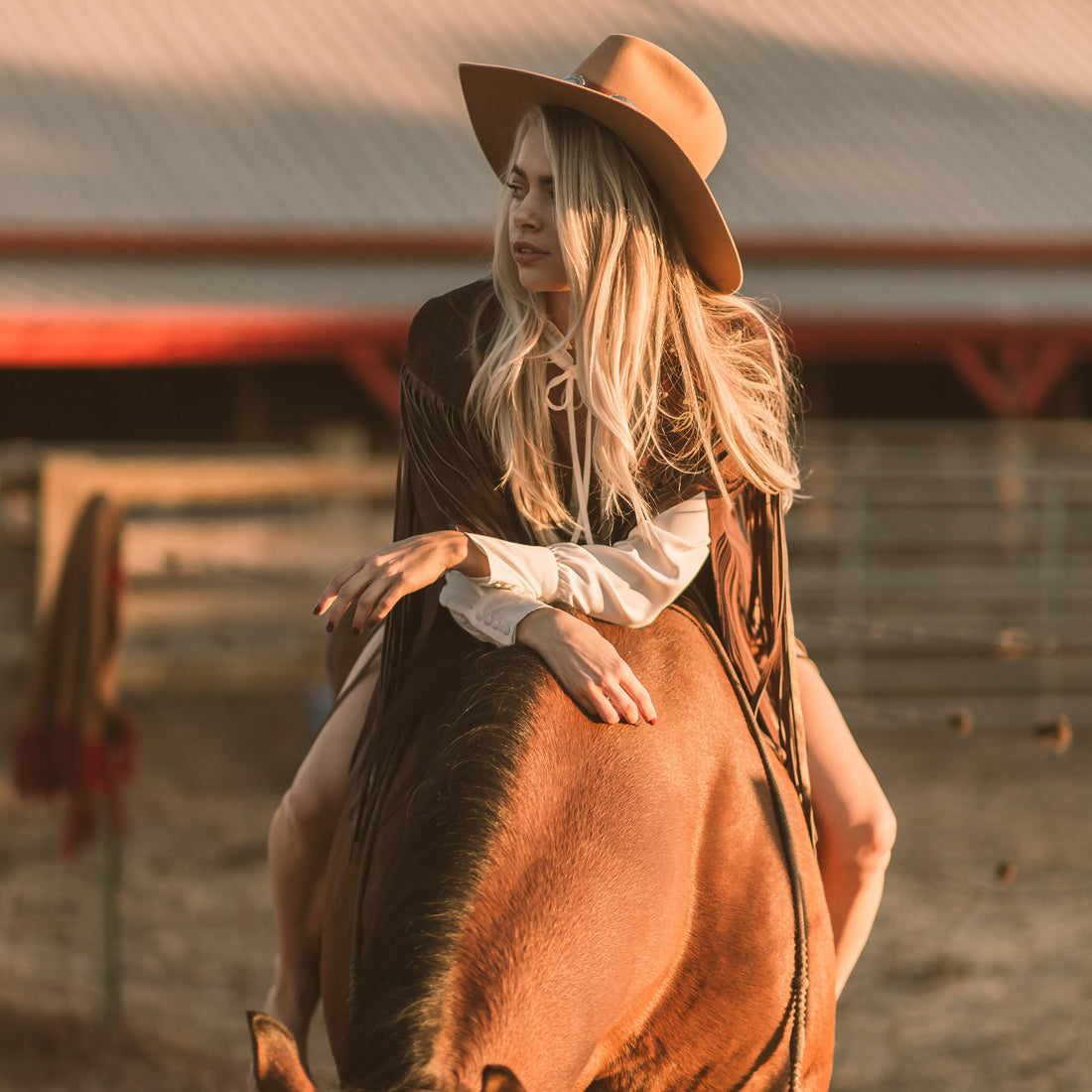 A woman wearing a brown suede cape with long metallic bronze fringe riding a horse
