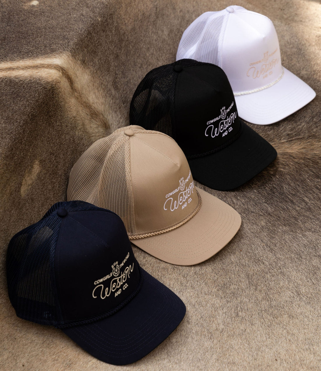A collection of snapback hats in black, white, beige, and  colors displayed on a surface with Western and Co logo