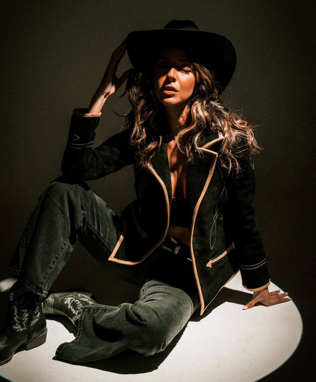 A woman wearing a black suede blazer with tan leather details paired with a black hat