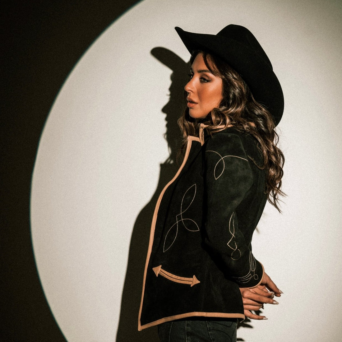A woman wearing a black suede blazer with tan leather details paired with a black hat
