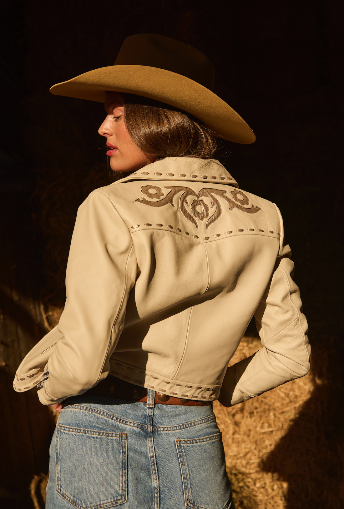 Woman in cowboy hat and white embroidered jacket by Western & Co in rustic setting 