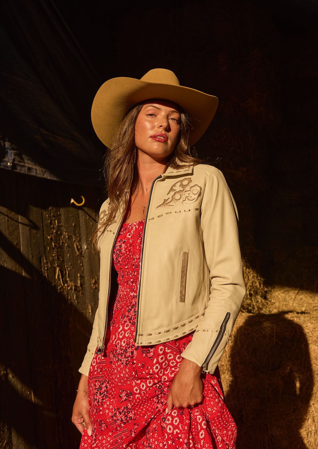 Woman in cowboy hat, red dress and a white embroidered jacket by Western & Co in rustic setting 