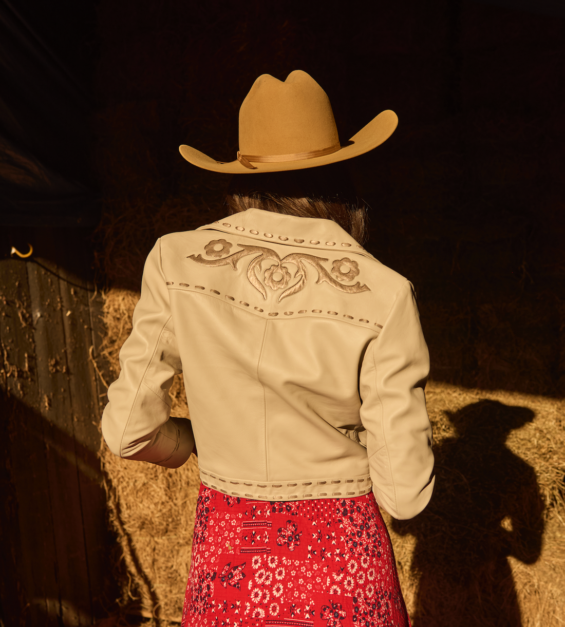 Woman in cowboy hat, red dress and a white embroidered jacket by Western & Co in rustic setting 