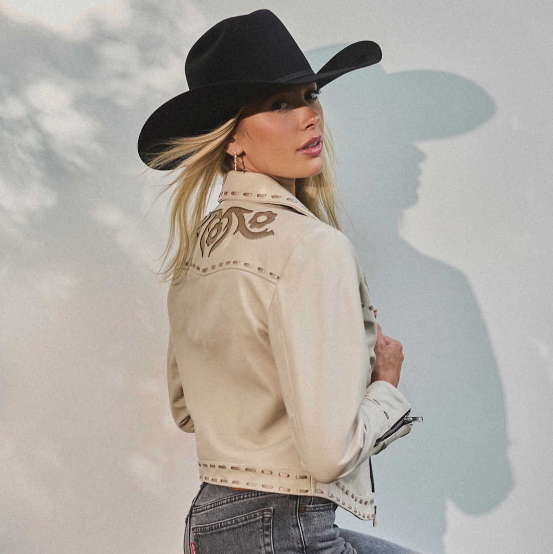 Woman in cowboy hat and white embroidered jacket by Western & Co against a light background 