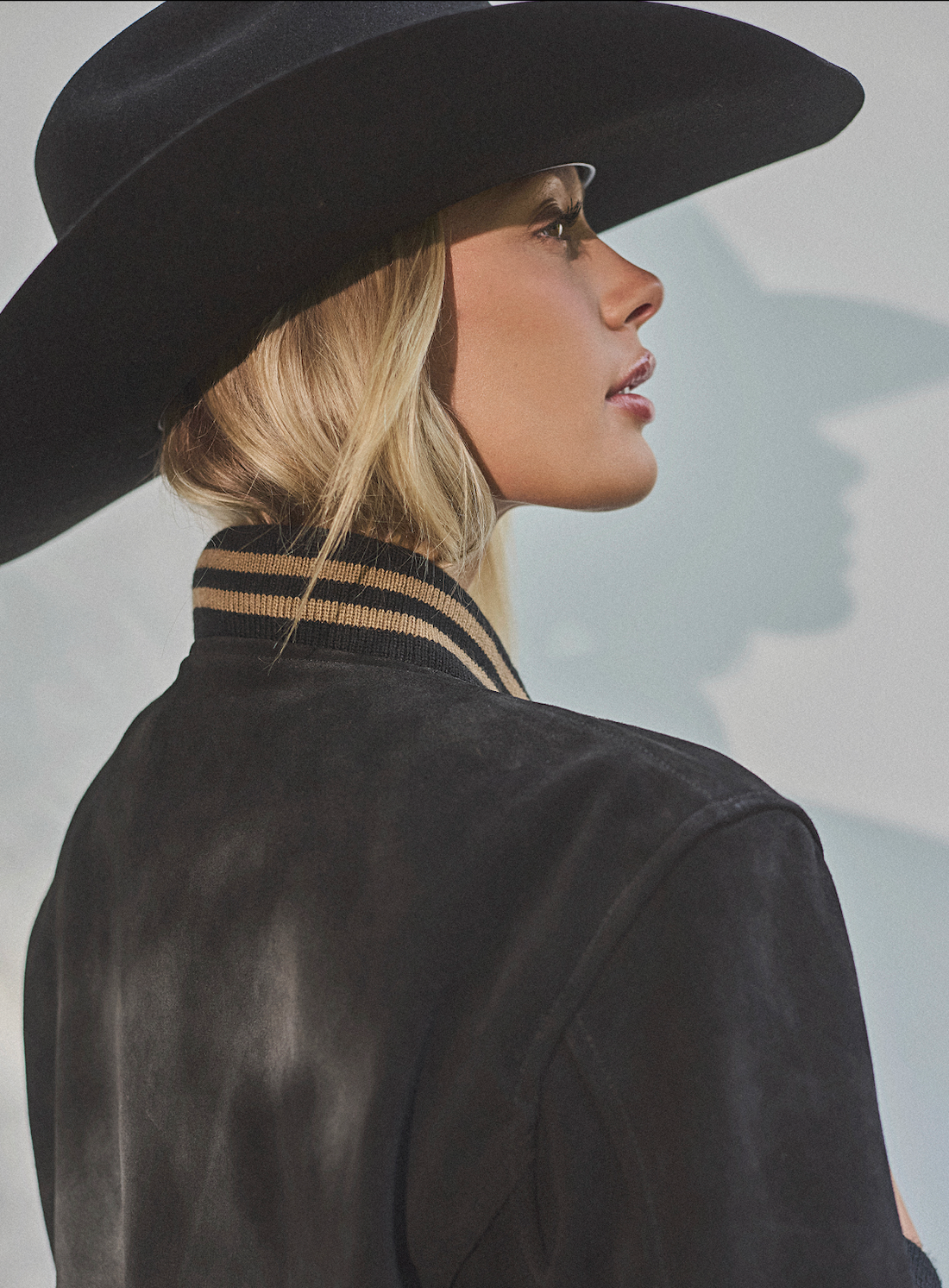 Woman in a cowboy hat wearing black embroidered bomber jacket by Western & Co against a light background 