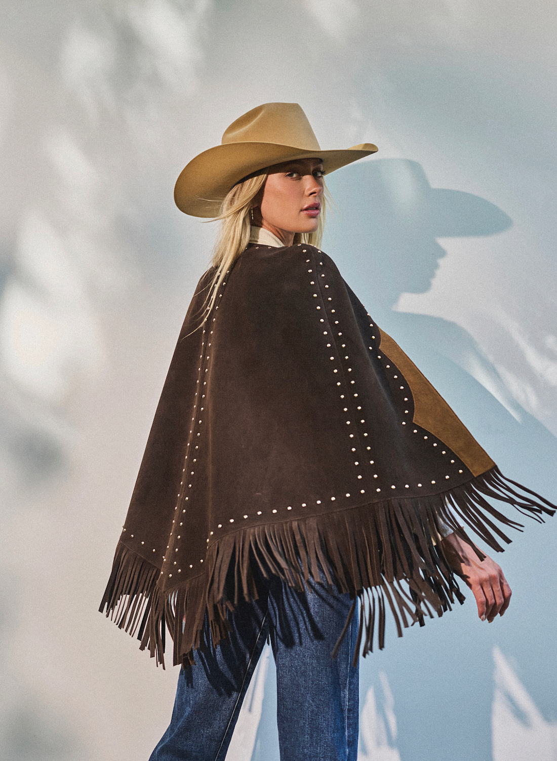 Woman wearing a cowboy hat and fringe studded cape by Western & Co