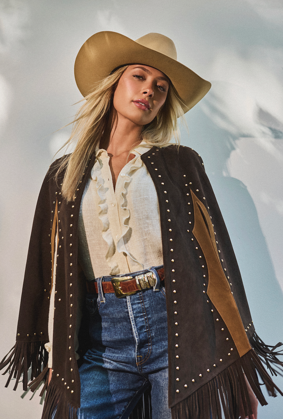 Woman wearing a cowboy hat and fringe studded cape by Western & Co 