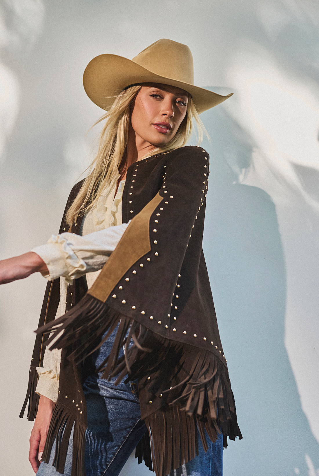Woman wearing a cowboy hat and fringe studded cape by Western & Co