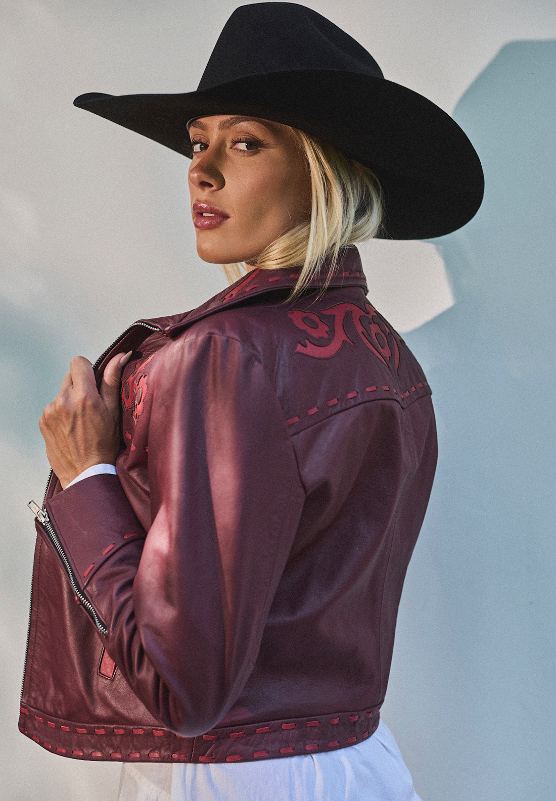 Woman in a cowboy hat wearing embroidered sangria jacket by Western & Co against a light background 