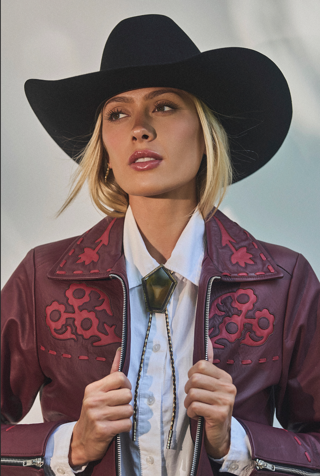 Woman in a cowboy hat wearing embroidered sangria jacket by Western & Co against a light background 