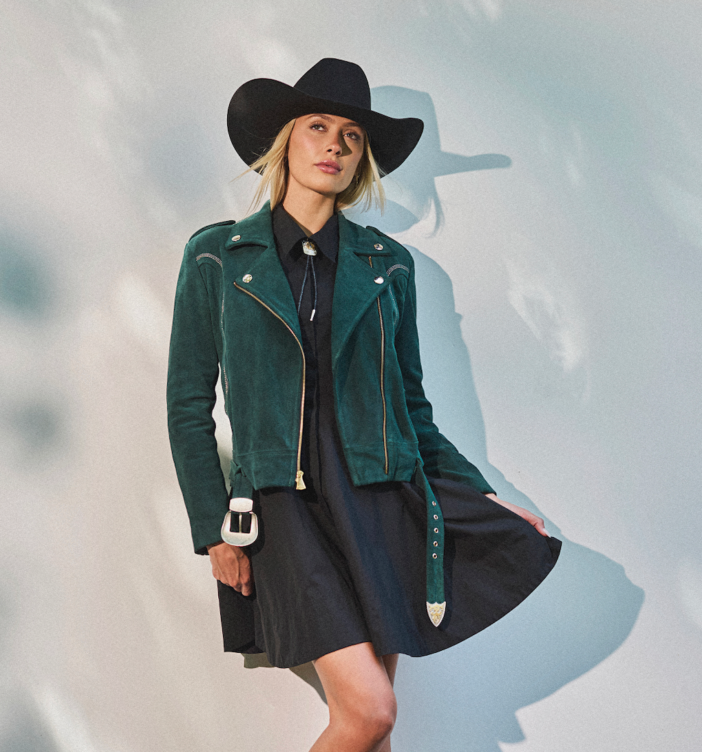Woman wearing cowboy hat and emerald green biker jacket by Western & Co against a light background