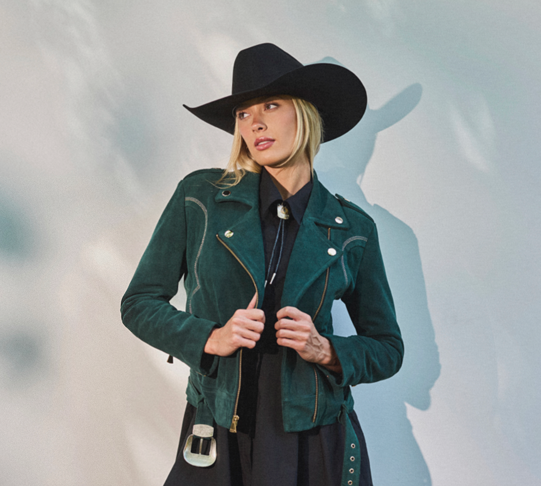 Woman wearing cowboy hat and emerald green biker jacket by Western & Co against a light background