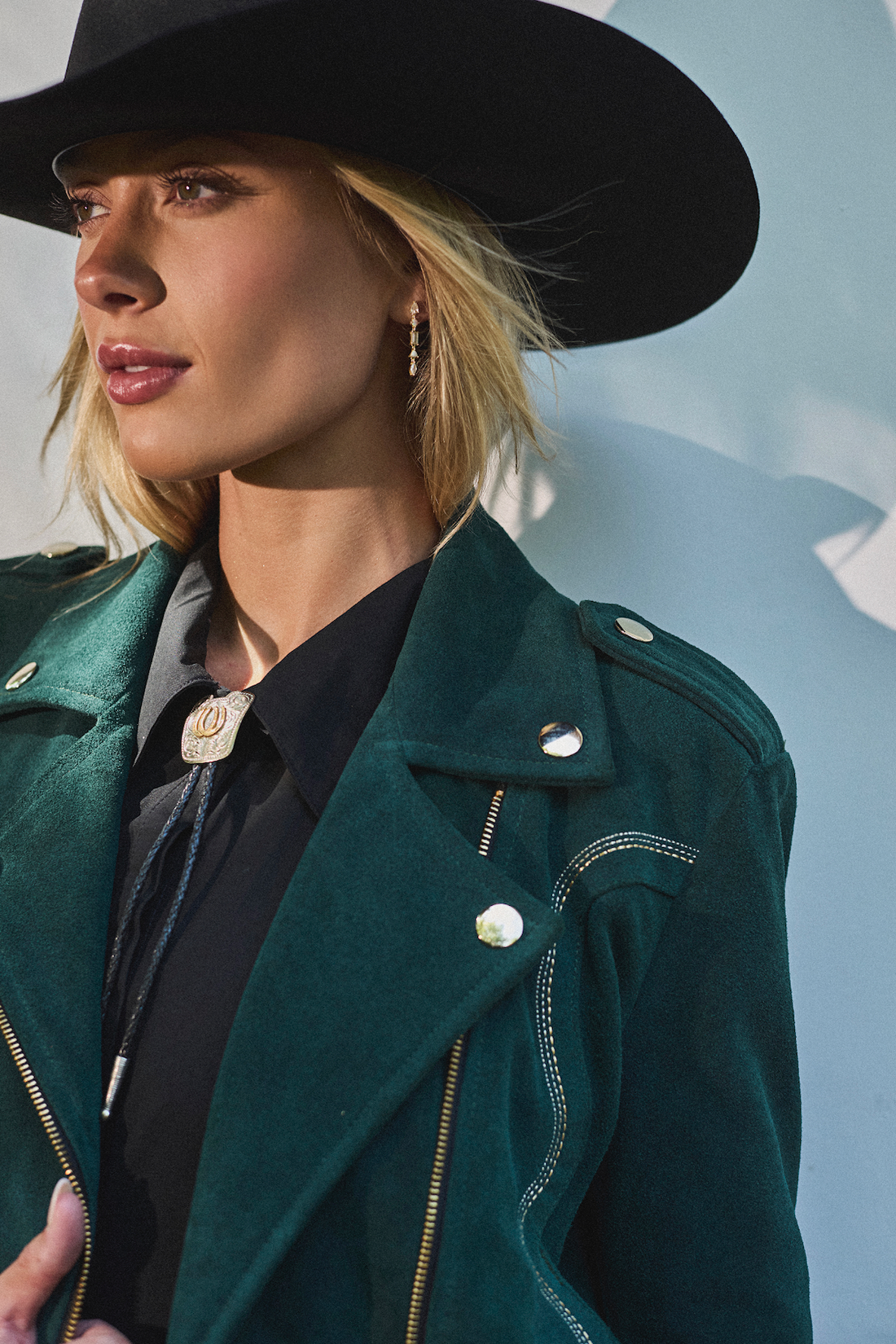 Woman wearing cowboy hat and emerald green biker jacket by Western & Co against a light background