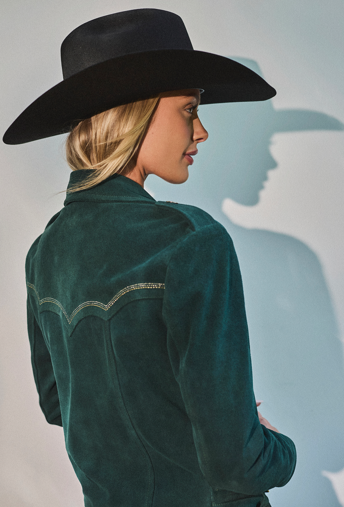 Woman wearing cowboy hat and emerald green biker jacket by Western & Co against a light background