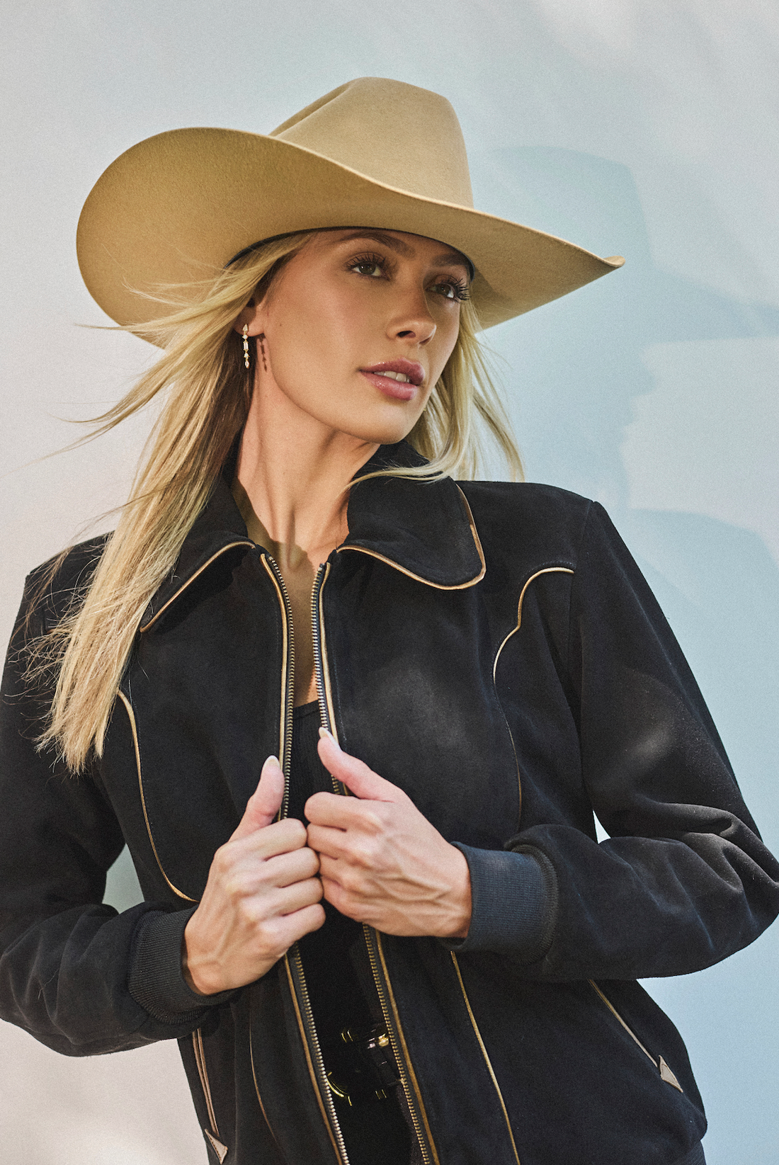 Woman in cowboy hat and black bomber jacket by Western & Co against a light background 