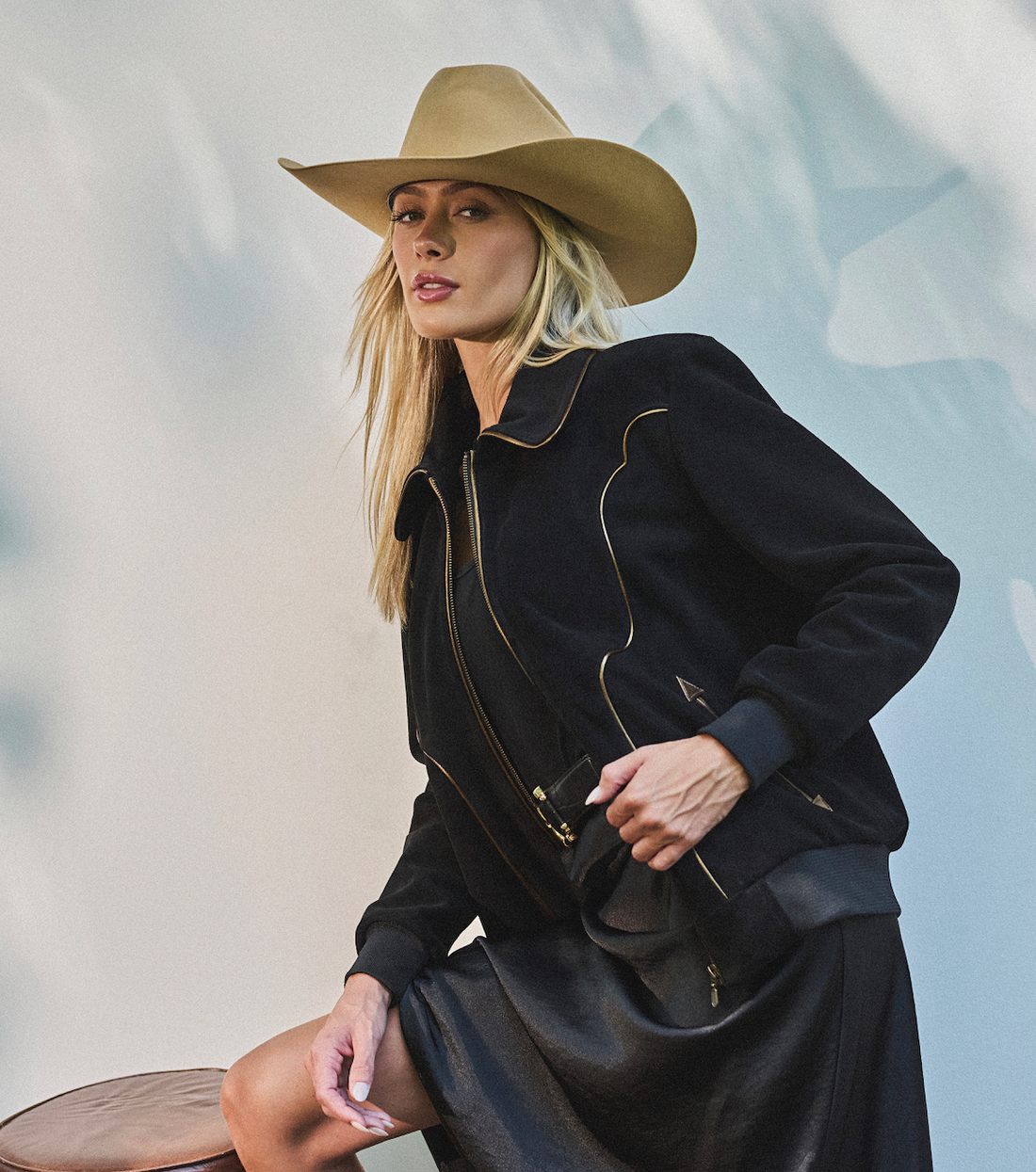 Woman in cowboy hat and black bomber jacket by Western & Co against a light background 
