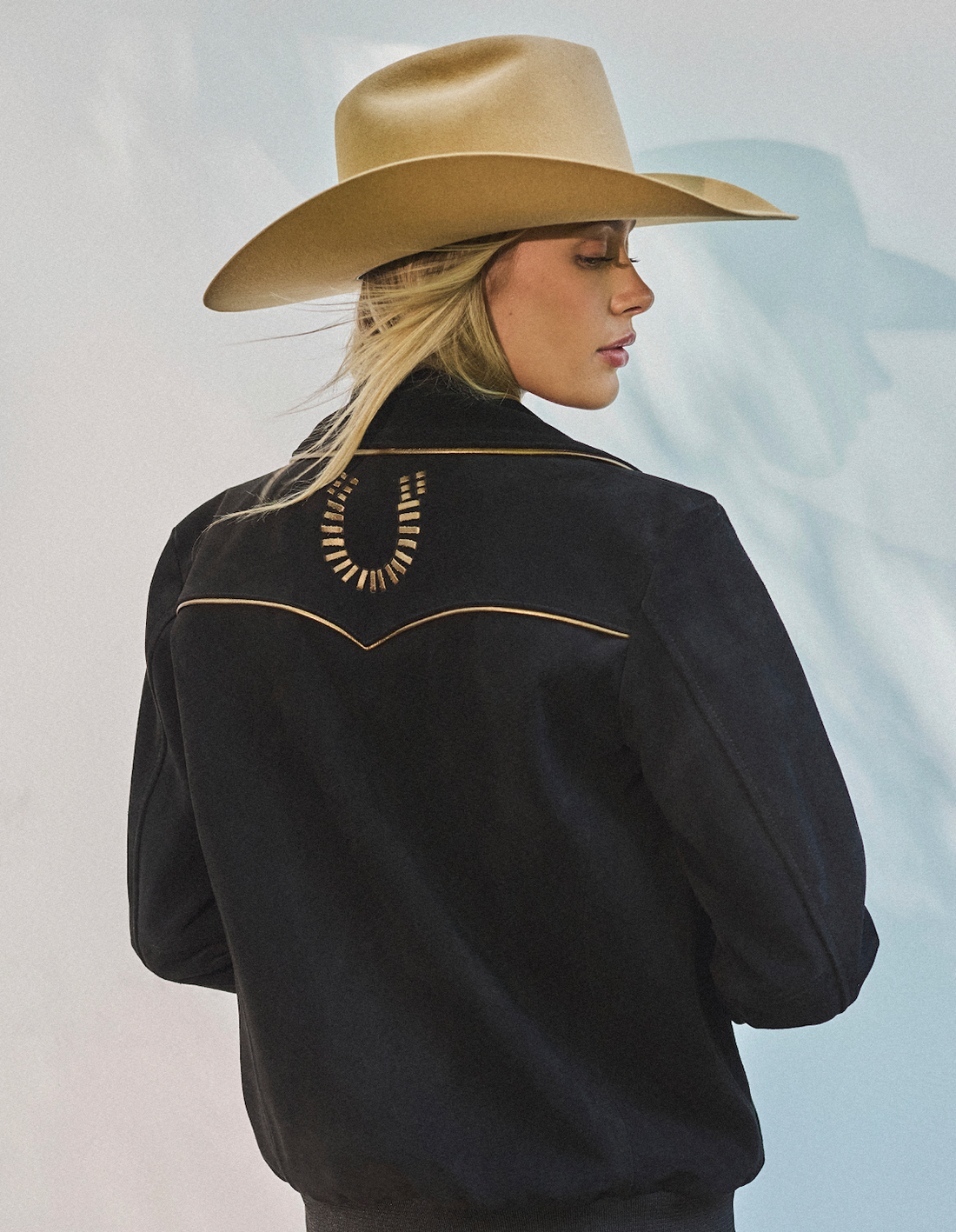 Woman in cowboy hat and black bomber jacket by Western & Co against a light background 
