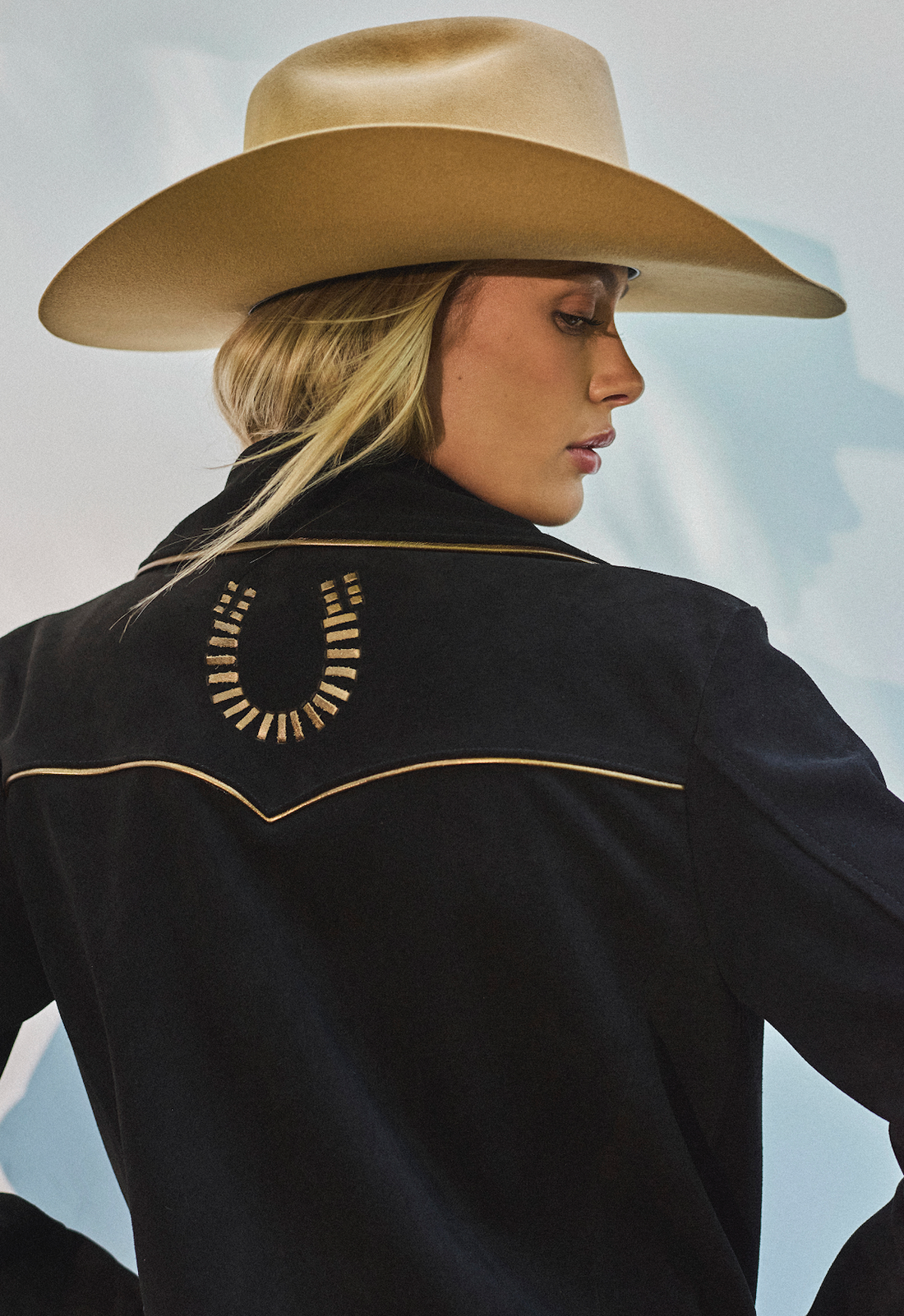 Woman in cowboy hat and black bomber jacket by Western & Co against a light background 
